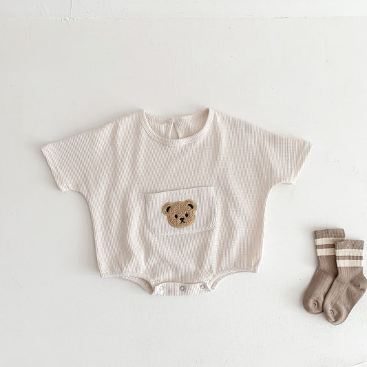 Toddler's beige waffle knit romper with bear patch pocket and beige striped socks on white background