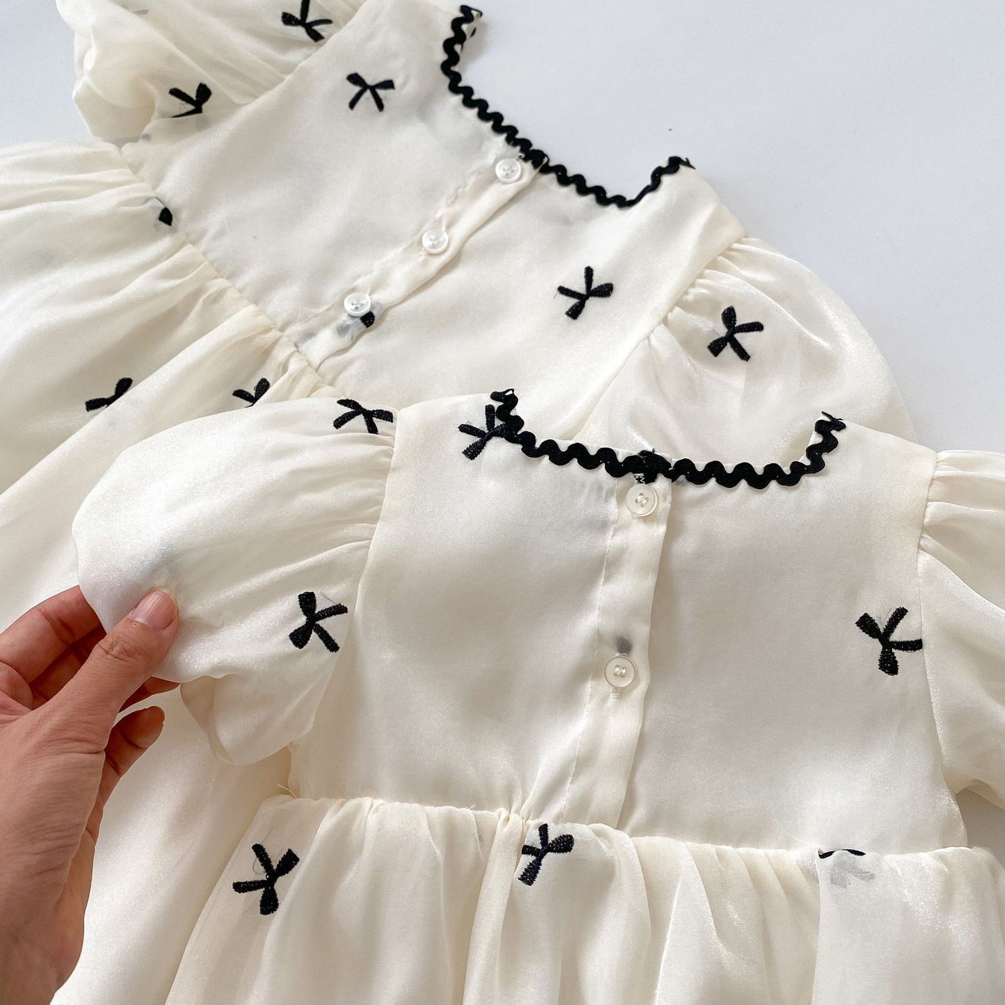 Toddleverse elegant white toddler dresses with black embroidered bows, puff sleeves, and button back