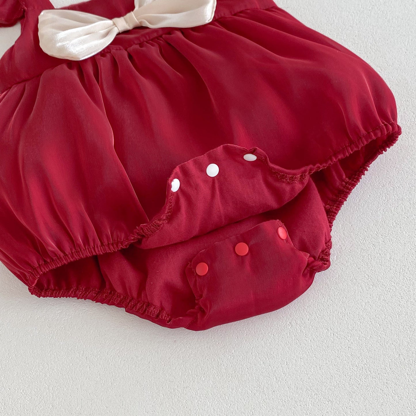 Red baby romper with white bow and snap buttons on a light background from Toddleverse