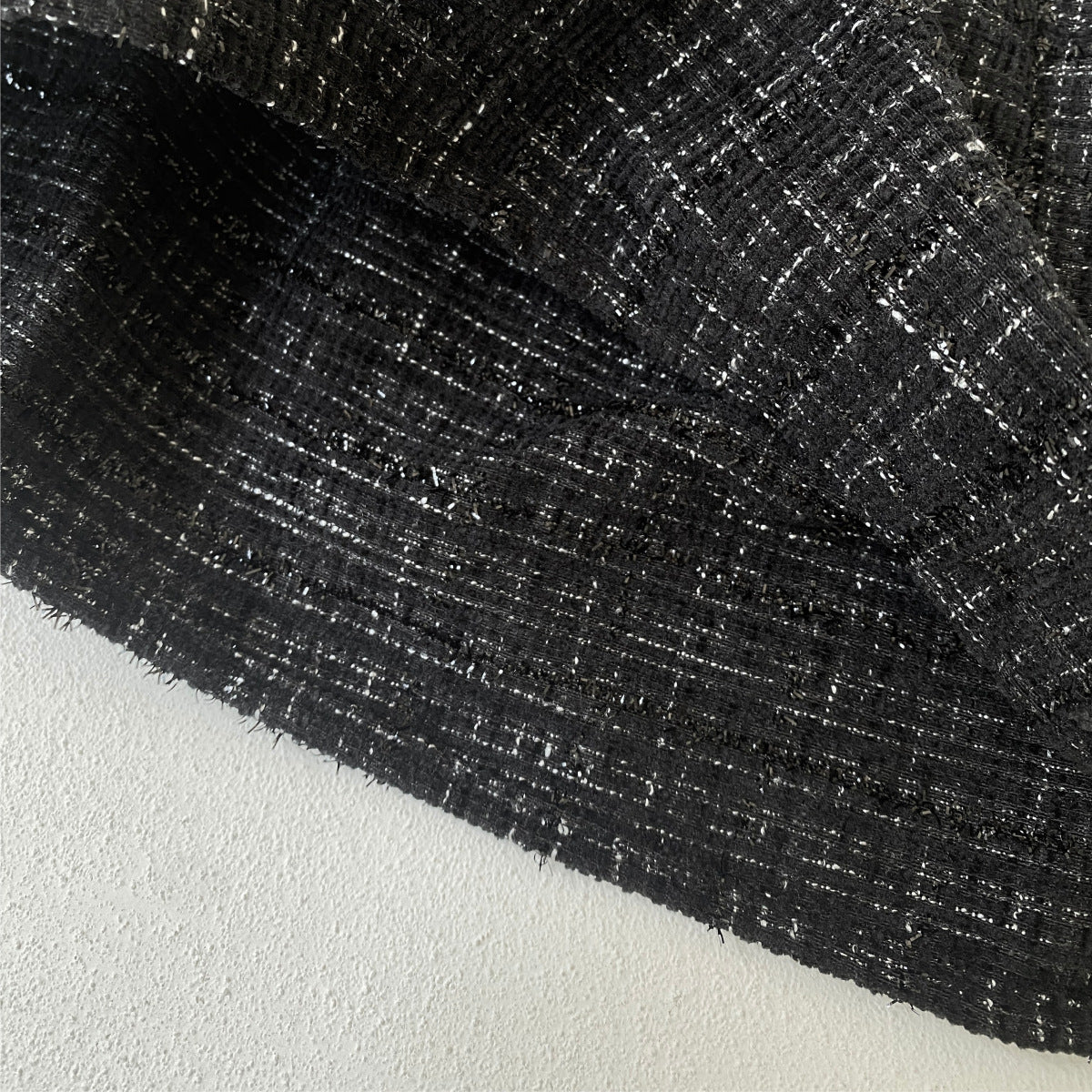Close-up of black tweed fabric with white specks and textured weave on light surface